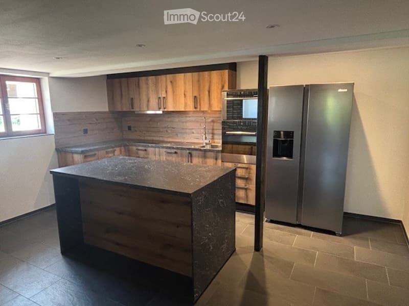 Modern kitchen with wood cabinetry, black granite countertop island, stainless steel appliances including a dishwasher, and tile flooring.