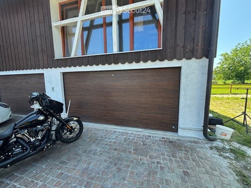 Two-story house with a large garage door, wooden exterior, and a motorcycle parked in front.