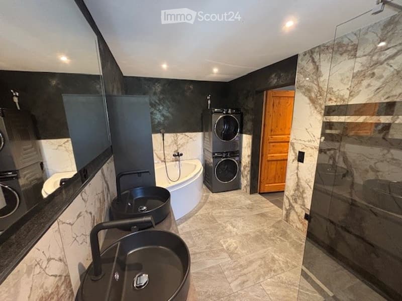 Large bathroom with marble-like tiles, freestanding bathtub, double vanity sinks, and laundry appliances including a washing machine and dishwasher