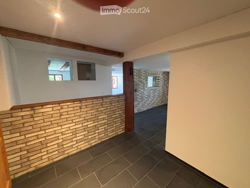 The image shows a room with white walls, a brick accent wall, and a tiled floor. There are wooden beams visible on the ceiling.