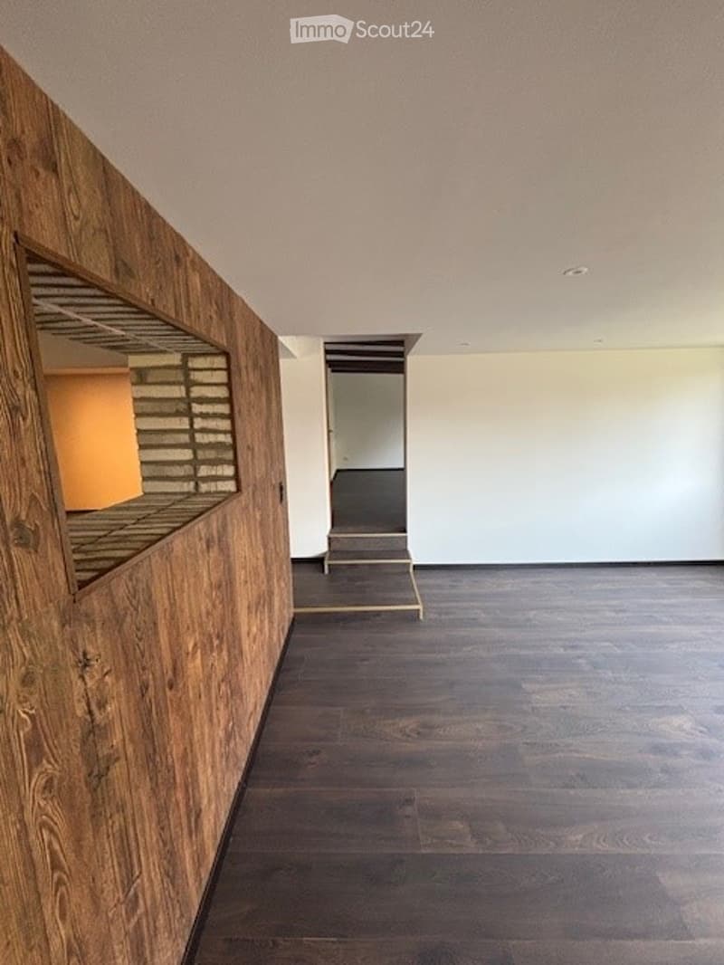 Large open living space with wooden accent wall, dark hardwood flooring, and a fireplace visible in the background.