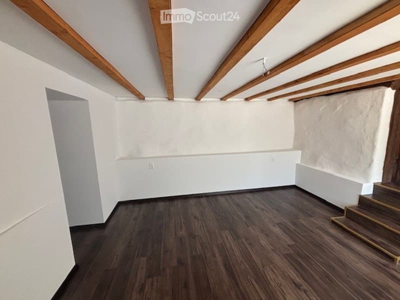 Empty room with wooden flooring, white walls, and exposed wooden beams on the ceiling. No furniture or equipment present.