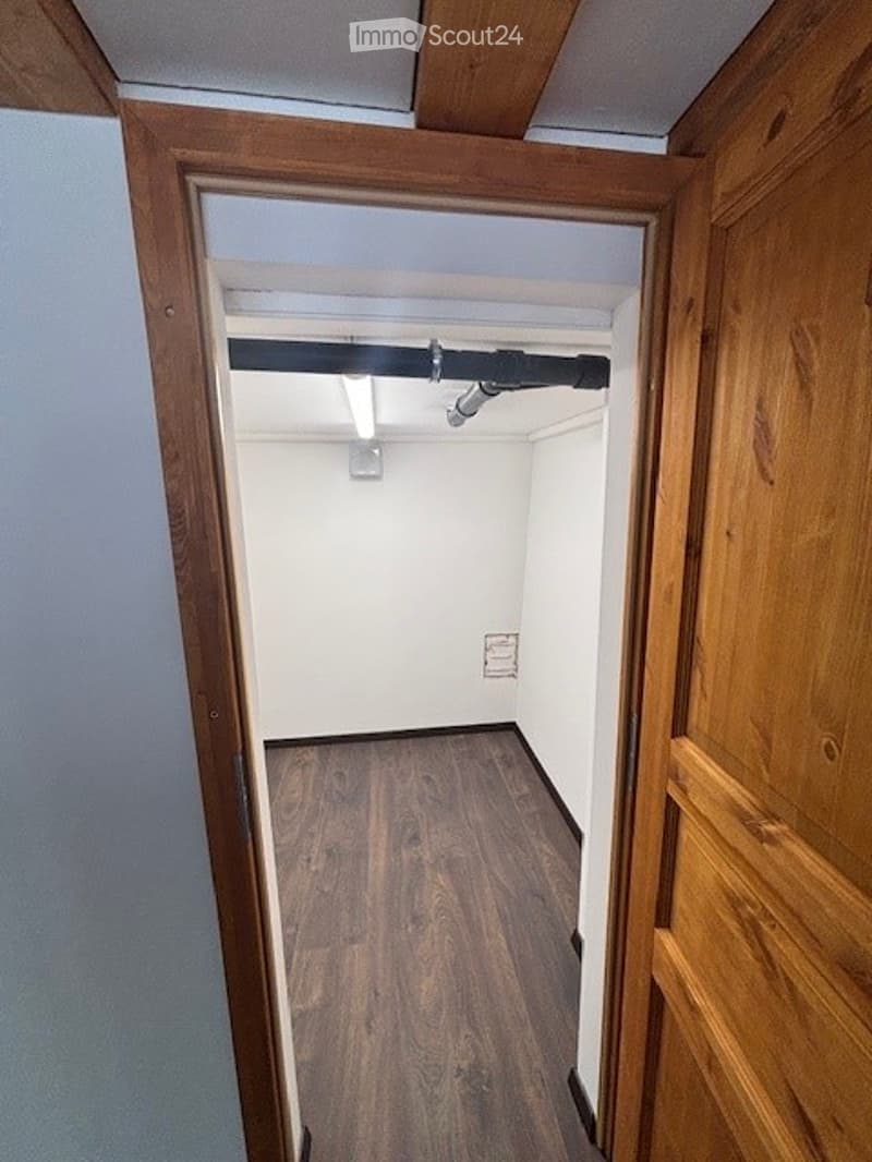 The image shows a small room with wooden walls and floors. There is a closet or storage space visible in the doorway, and the room appears to have a simple, minimalist design.