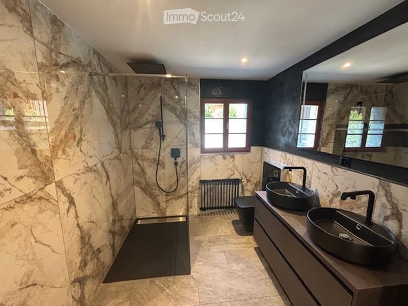 Large bathroom with marble-like tiles covering the walls, a walk-in shower, and two vessel sinks on a dark vanity counter