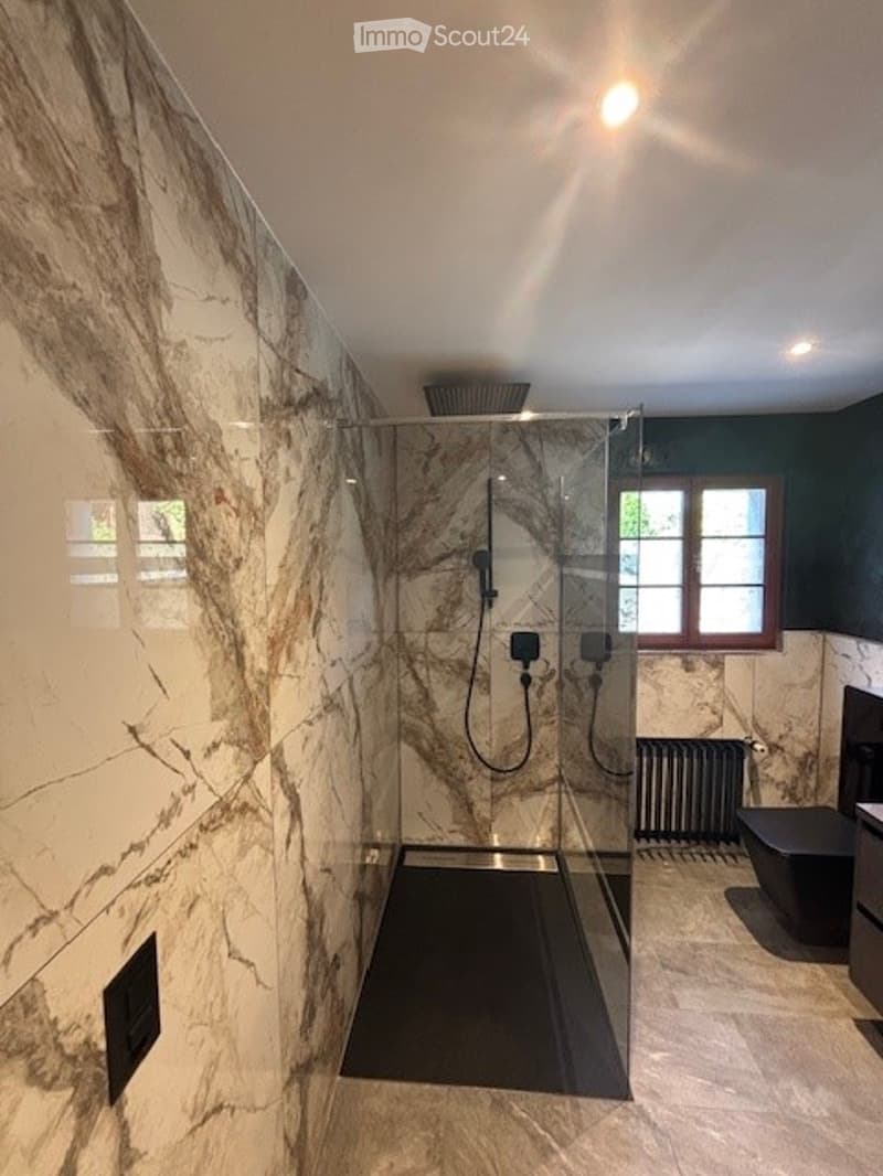 Large bathroom with marble-like tile walls, a walk-in shower with a rainfall showerhead, and a black tiled floor.