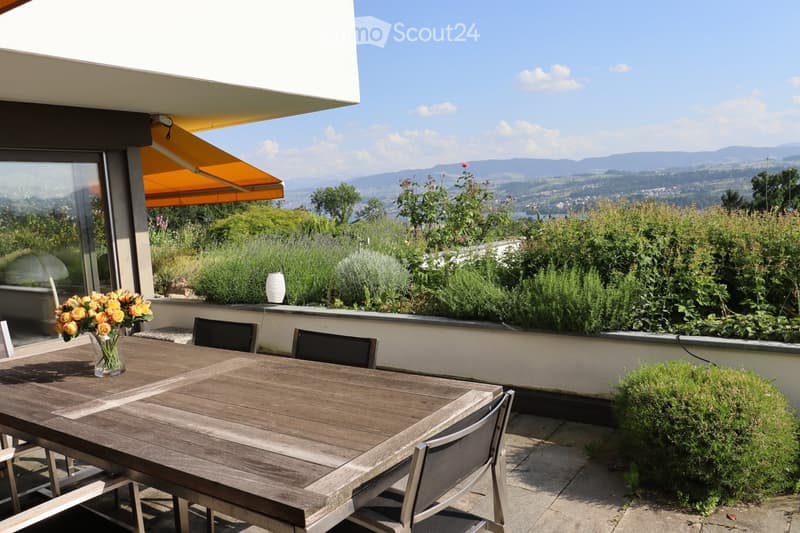 Balcony with wooden table, chairs, vase of flowers, and scenic mountain view.