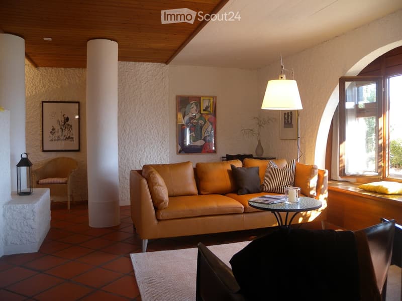 Cozy living room with leather sofa, coffee table, artwork on the walls, and a fireplace. The room has a warm, inviting atmosphere with natural light coming in through the windows.