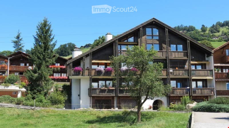 3-story wooden apartment building with balconies, surrounded by trees and greenery in a mountainous, rural setting