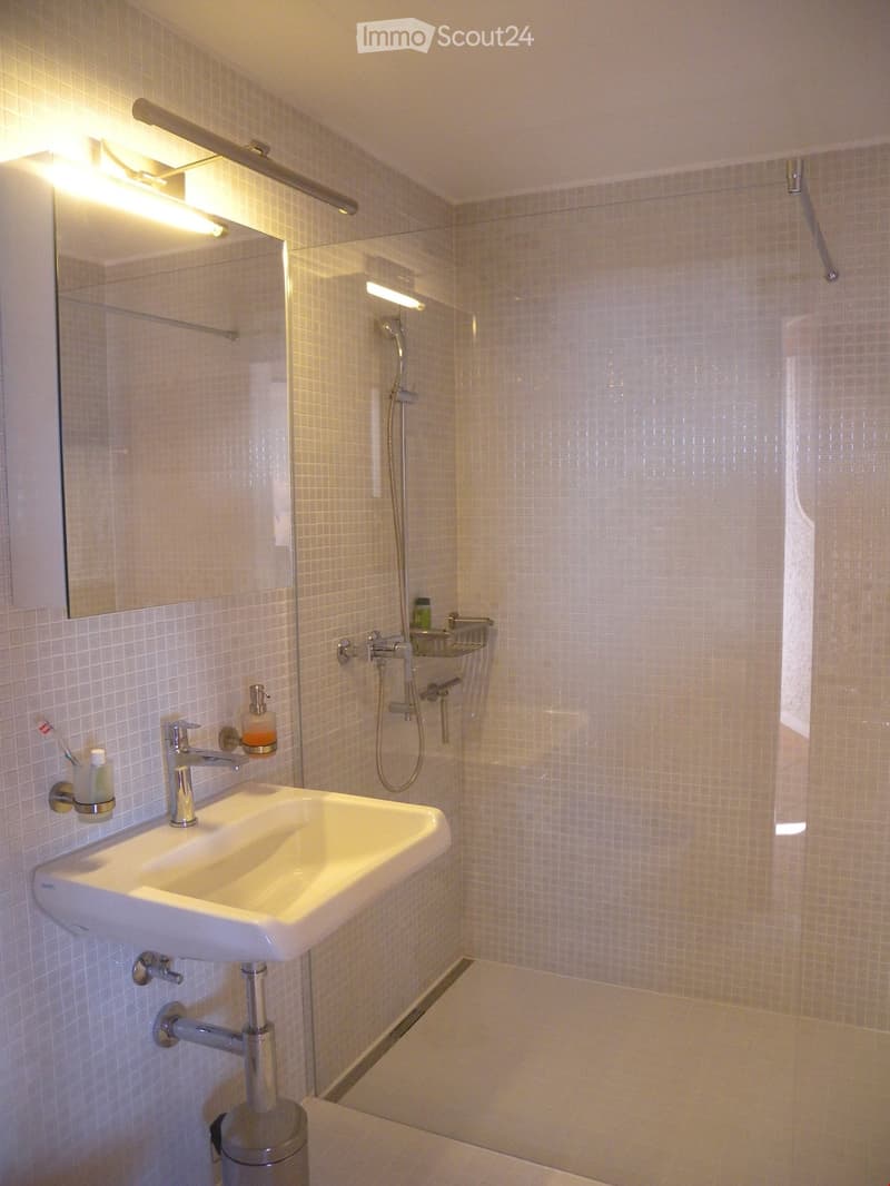 Bathroom with white tile walls, a sink, and a shower area with a glass door.