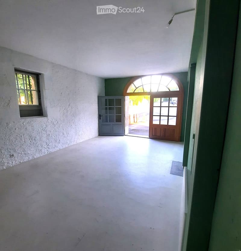 Empty hallway with white walls, a single window on the left, and two doors at the end leading outside.