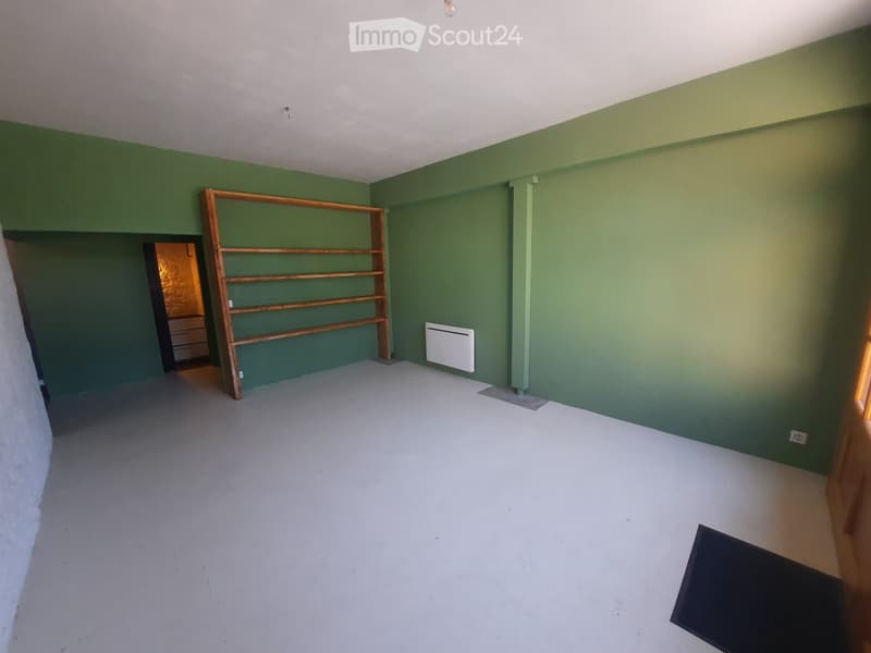 Empty room with green walls, white floor, wooden shelf, radiator, and a doorway leading to another room.