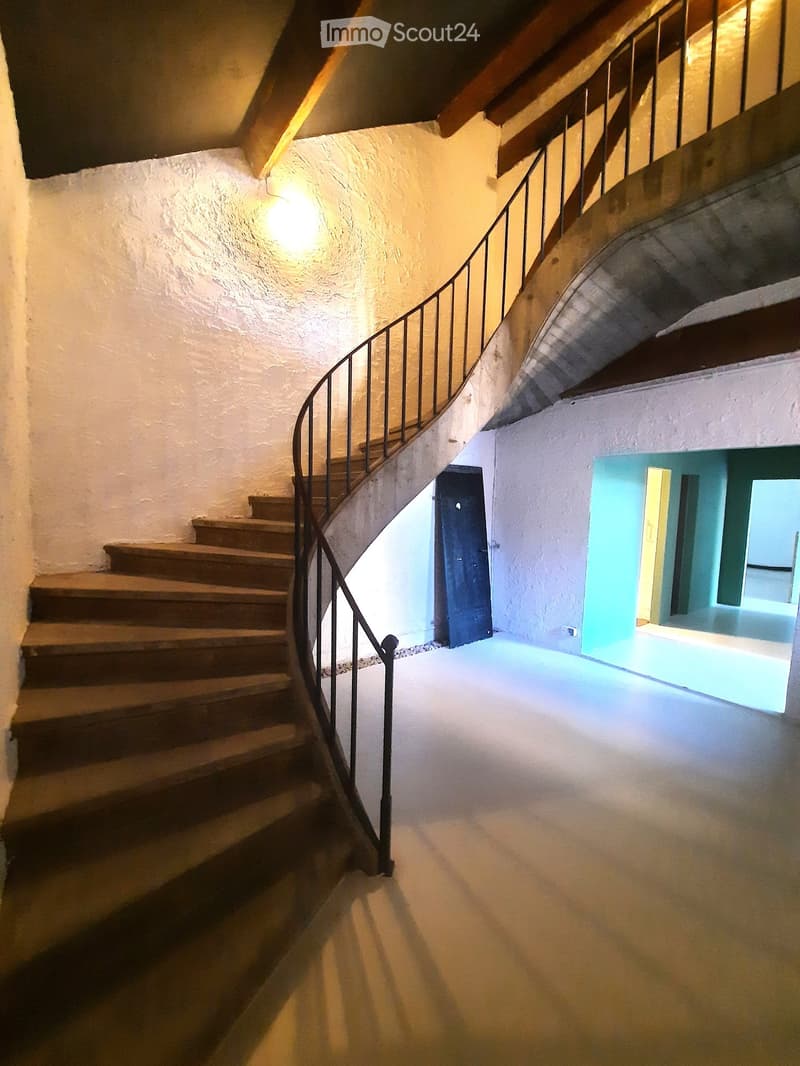 Staircase with wooden steps and metal railing, leading to a brightly lit room with white walls and a blue accent wall.