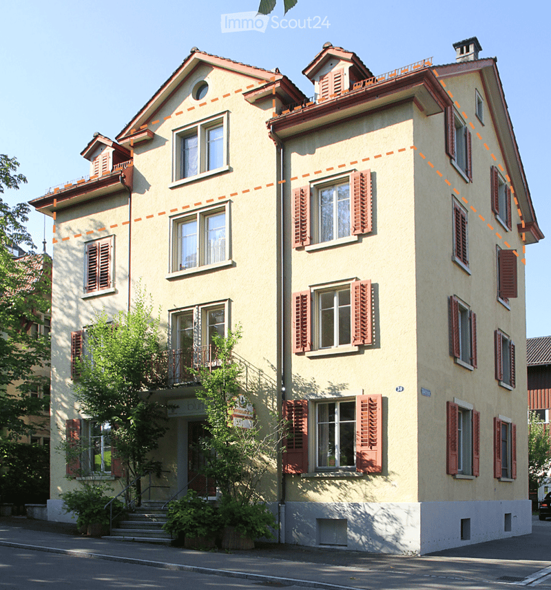 A multi-story residential house with light yellow walls, red shutters, and multiple windows. Features include a balcony on the second floor, a small garden area, and a staircase leading to the entrance.