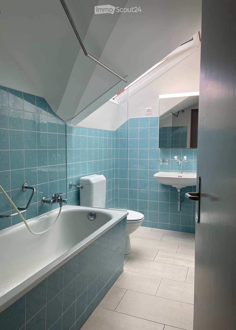 Modern bathroom with blue tiles, white bathtub, toilet, sink, and mirror. Features a skylight window for natural light.