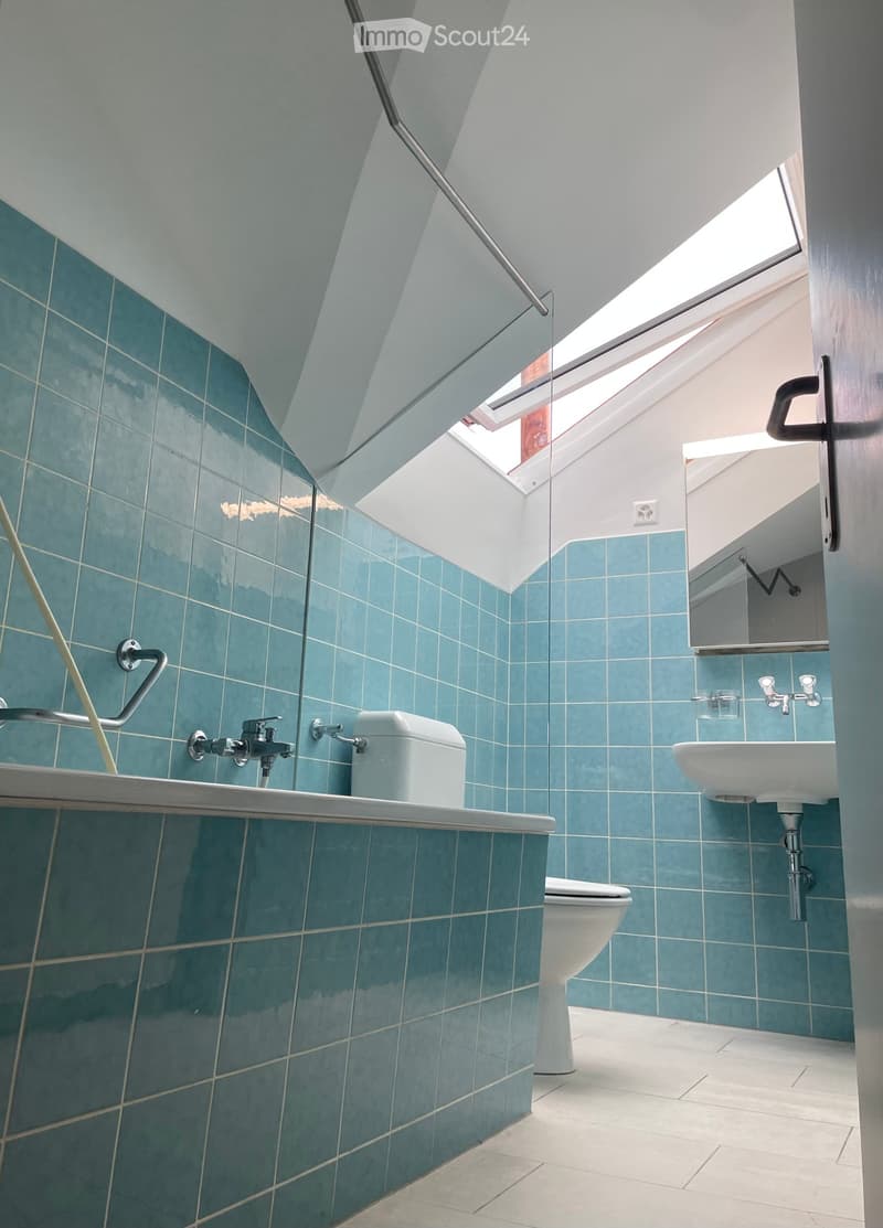 Modern bathroom with blue tiles, white fixtures, and a skylight window providing natural light.