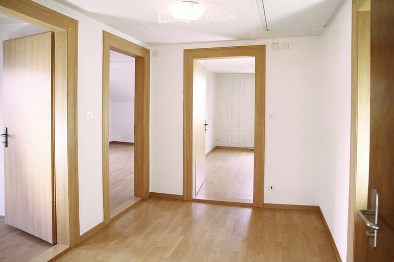 Empty hallway with wooden flooring, white walls, and multiple doors leading to other rooms.