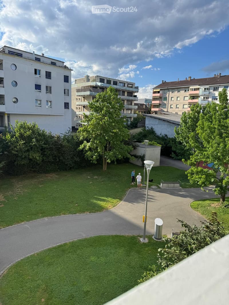 Courtyard view with green lawns, pathways, trees, and surrounding residential buildings with balconies.