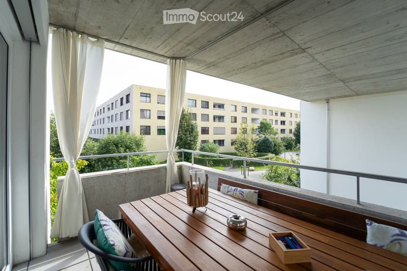 Balcony with wooden table, chairs, bench, cushions, candle holder, and small wooden box.