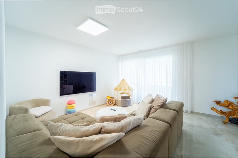 Modern living room with a large sectional sofa, coffee table, flat-screen TV, and a small play tent for children.