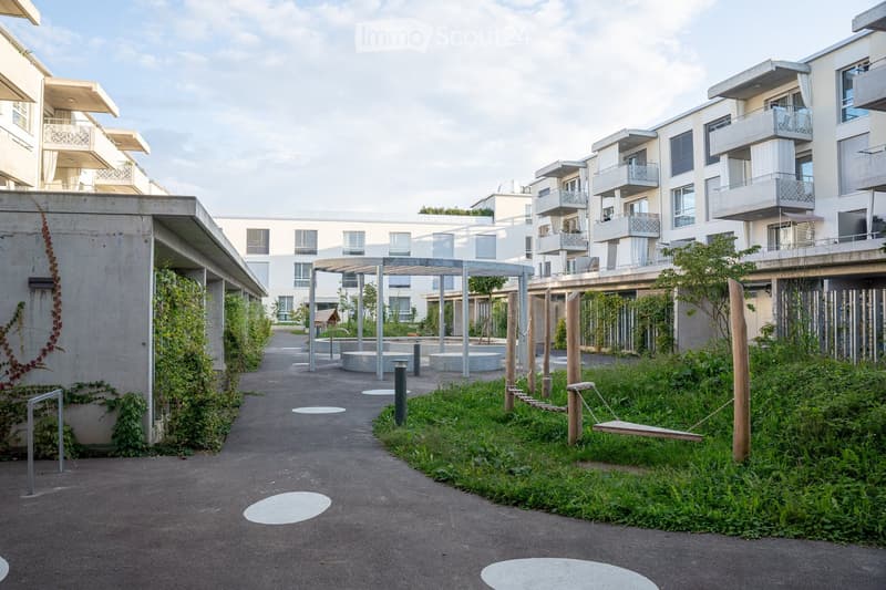 Courtyard area with modern apartment buildings, greenery, a swing, and seating areas.