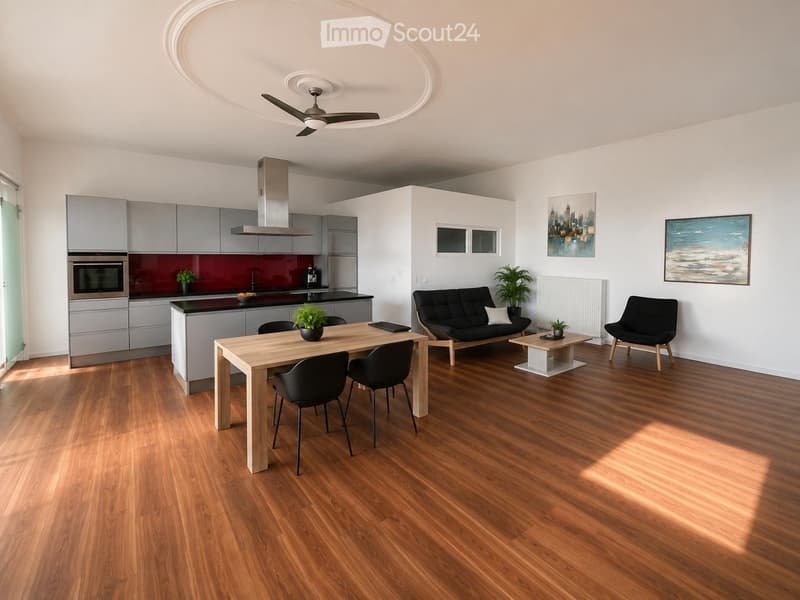 Modern open-plan living and dining area with wooden flooring, grey cabinets, a black sofa, a wooden dining table with chairs, and a small kitchen area with an oven and faucet.