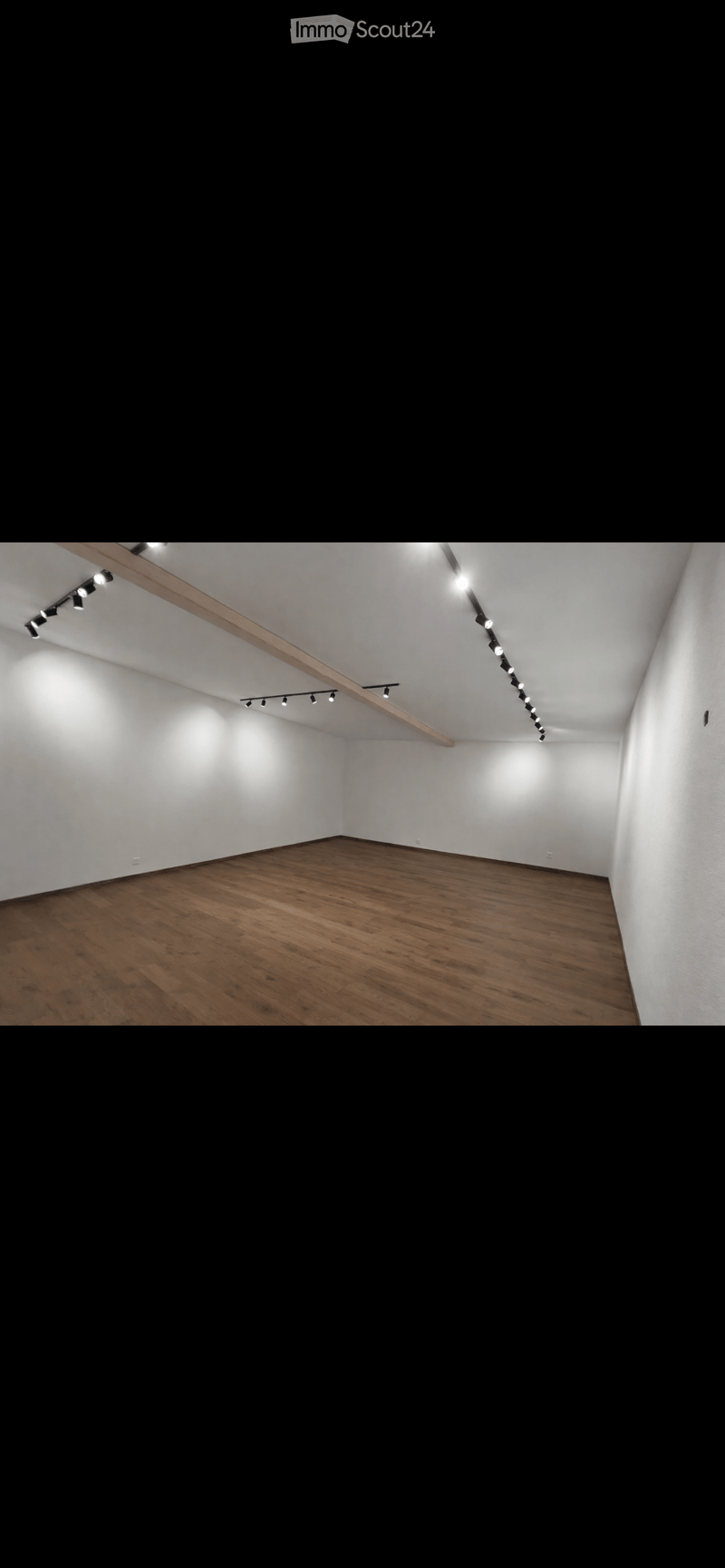 Empty room with wooden flooring and white walls, featuring track lighting mounted on the ceiling.