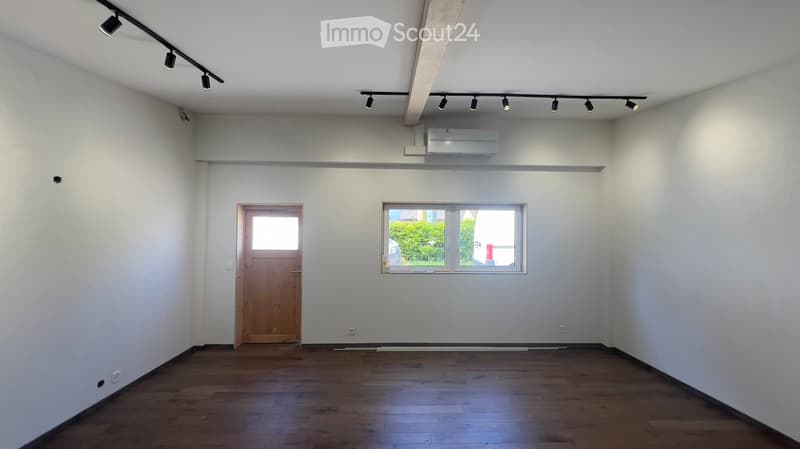 Empty room with wooden flooring, white walls, a single window, and a wooden door.