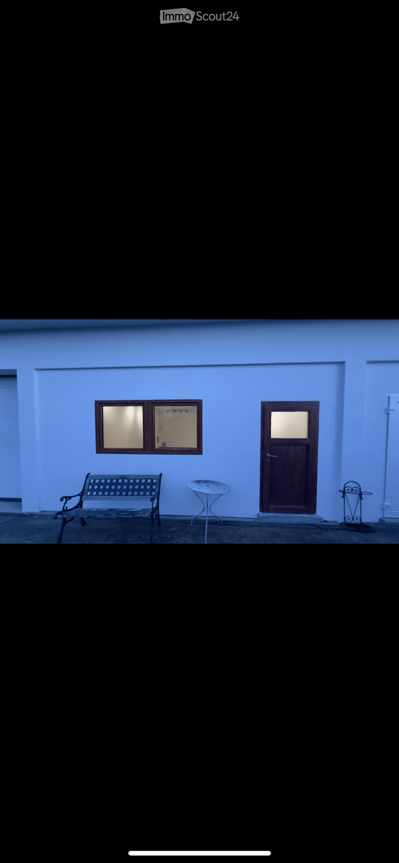 A small outdoor area with a bench, a small table, and a door with a window. The walls are painted light blue.