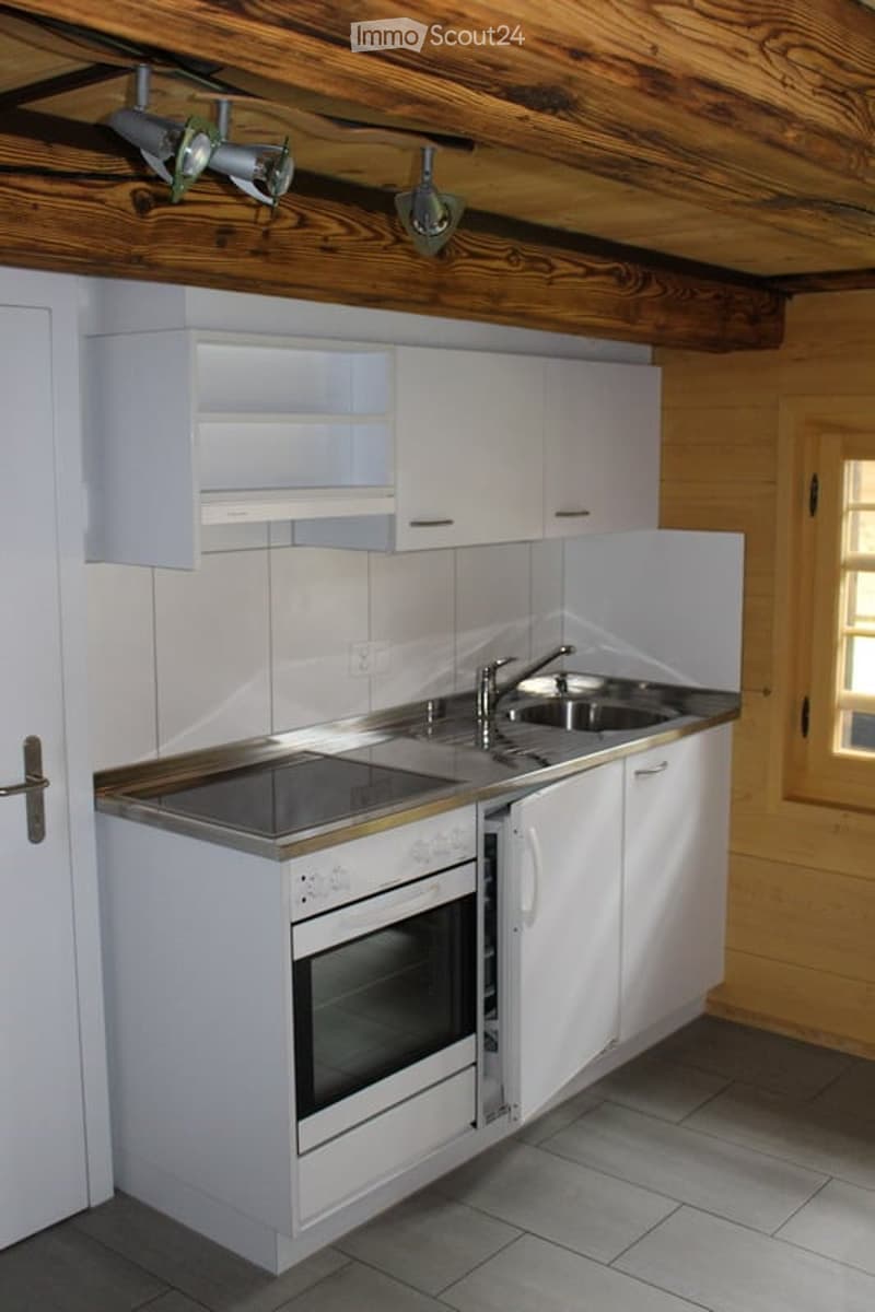Modern kitchen with white cabinets, stainless steel sink, and built-in oven. Exposed wooden ceiling beams and warm lighting.