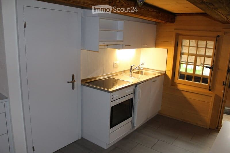 Compact kitchen with white cabinets, a built-in oven, a sink with a faucet, and a window with wooden framing.