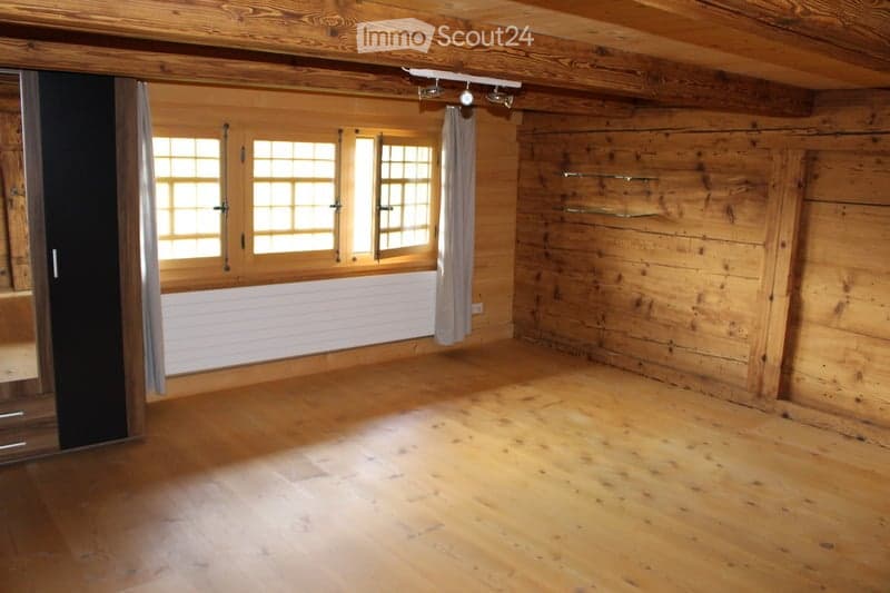 Empty room with wooden walls and floor, large windows with white frames, and a radiator below the windows. No furniture or equipment present.