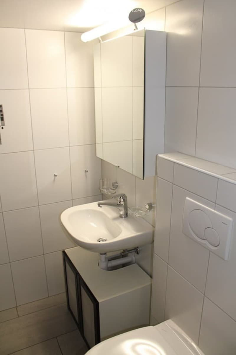 Modern bathroom with white tiles, a sink, mirror, and cabinet.