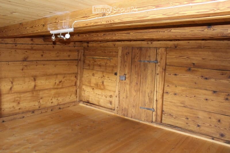 Empty wooden room with exposed wooden walls, ceiling, and floor. Features built-in wooden cabinets with metal handles and a small light fixture on the wall.