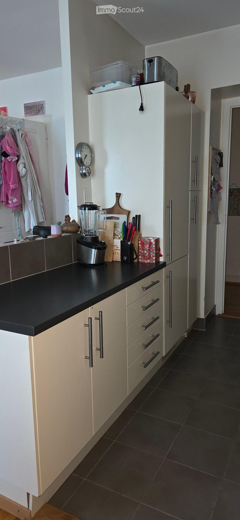 Modern kitchen with white cabinets, black countertop, stainless steel appliances, and various kitchen items on the counter.