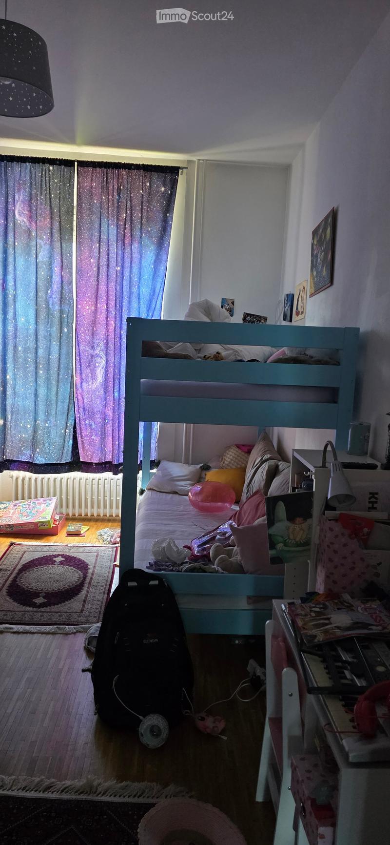A cozy bedroom with a bunk bed, colorful pillows, a backpack, a small table, and a rug on the floor.