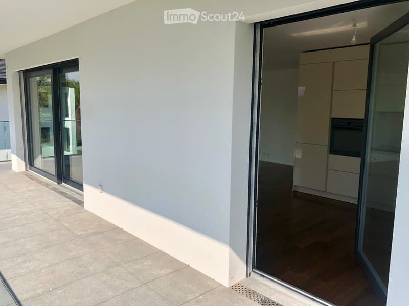 Modern balcony with large sliding glass doors leading to a kitchen area, tiled floor, and white walls.