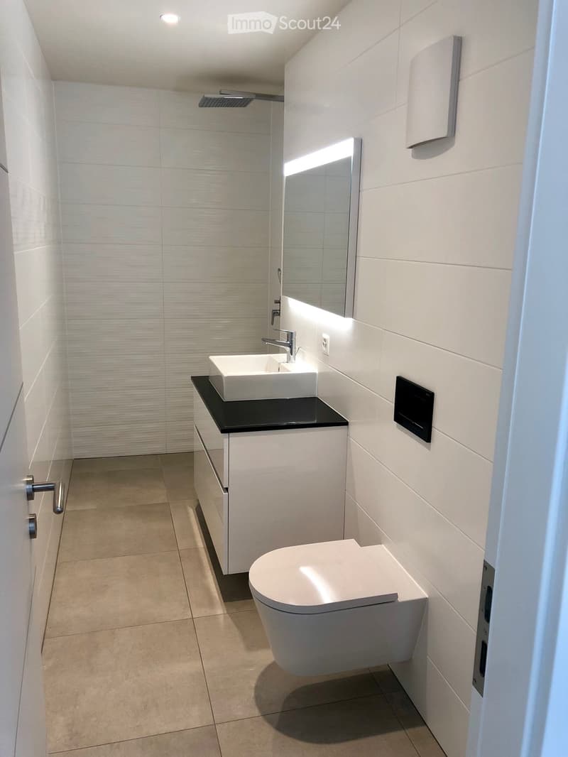 Modern bathroom with white tiles, a sink with a black countertop, a toilet, a mirror, and a cabinet.