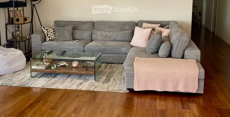 Modern living room with a grey sectional sofa, glass coffee table, wooden floor, and decorative pillows.