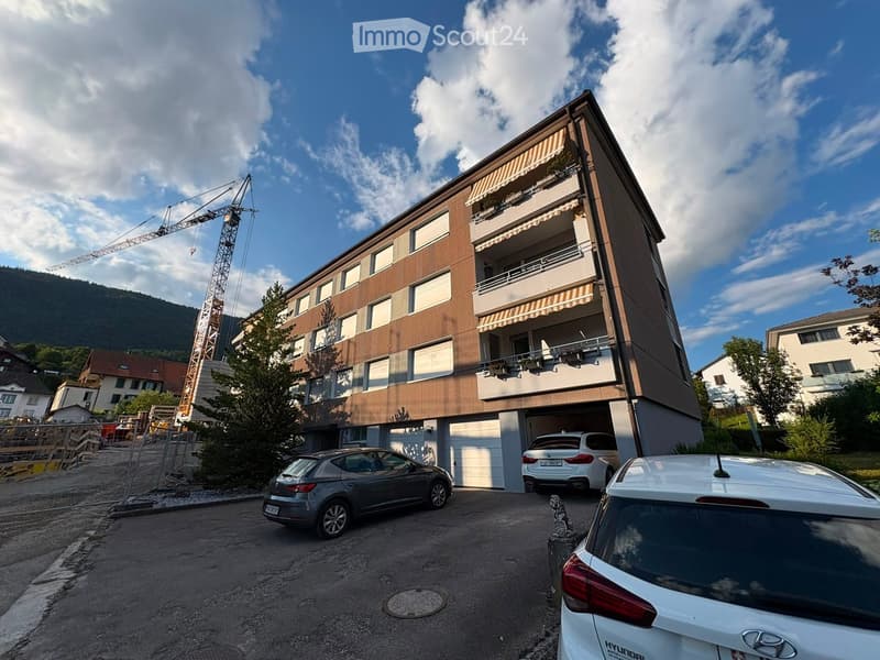 Modern multi-story building with balconies, garage, and several parked cars in front.