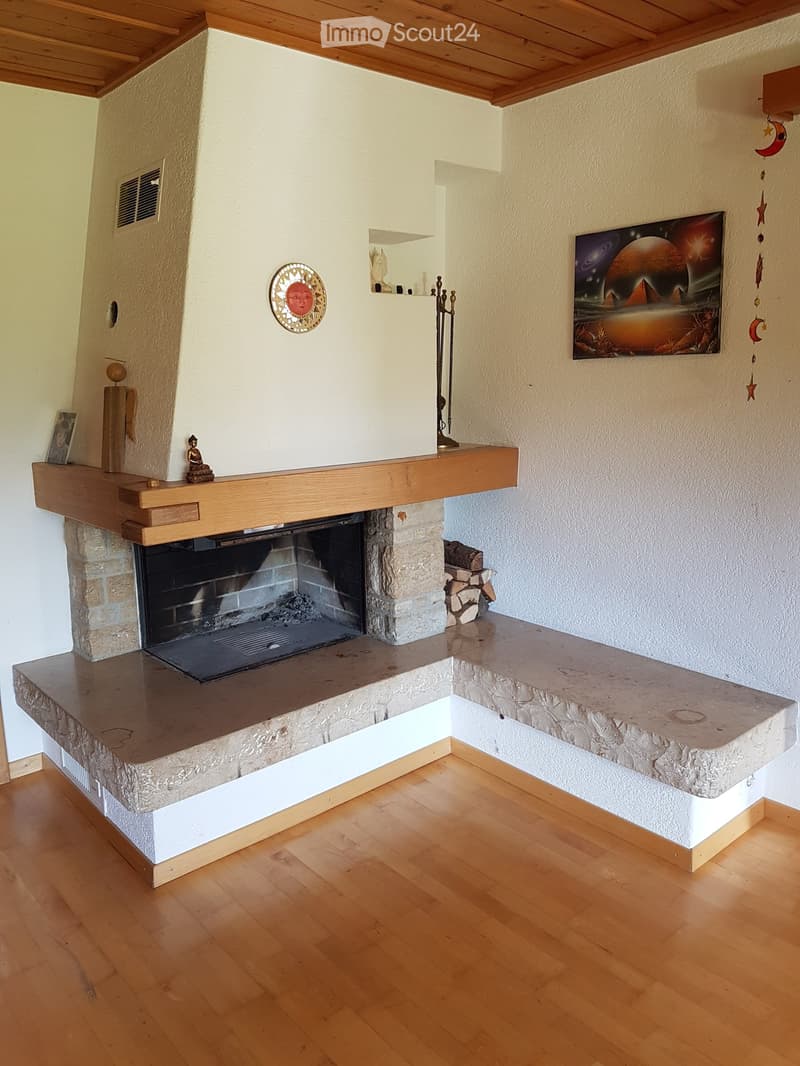 Living room with a stone fireplace, wooden mantel, decorative items on mantel, and a painting on the wall.
