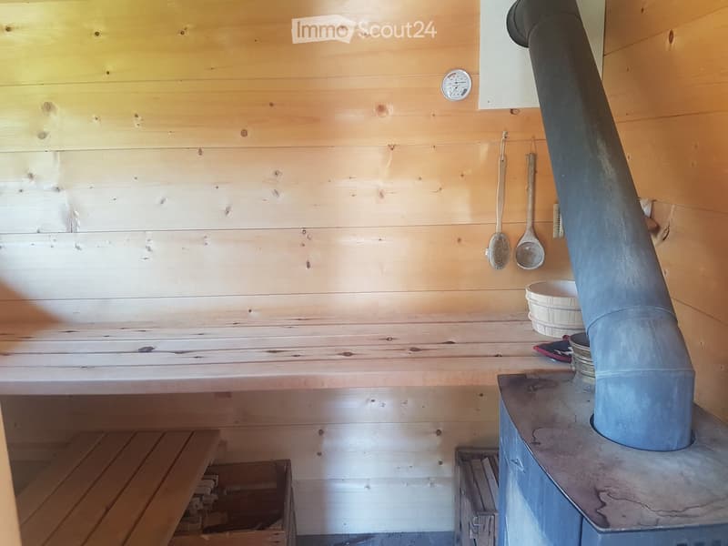 Wooden sauna interior with a bench, thermometer, and sauna accessories like a wooden spoon, brush, and bowl.