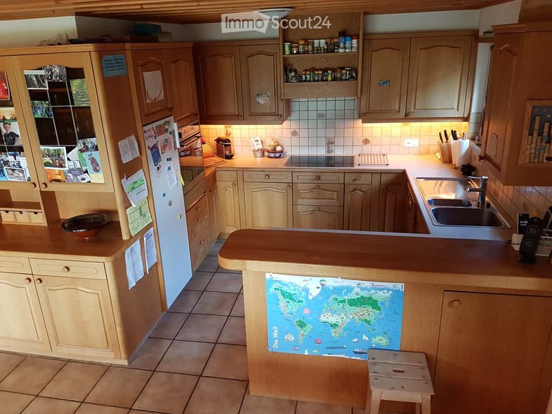 Bright kitchen with wooden cabinets, a central island, a sink, and various appliances. A world map is placed on the island, and a small stool is nearby.