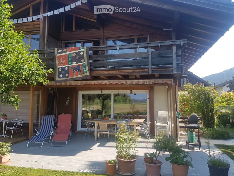 Outdoor patio with wooden furniture, potted plants, barbecue, and a covered balcony area with a decorative tapestry.