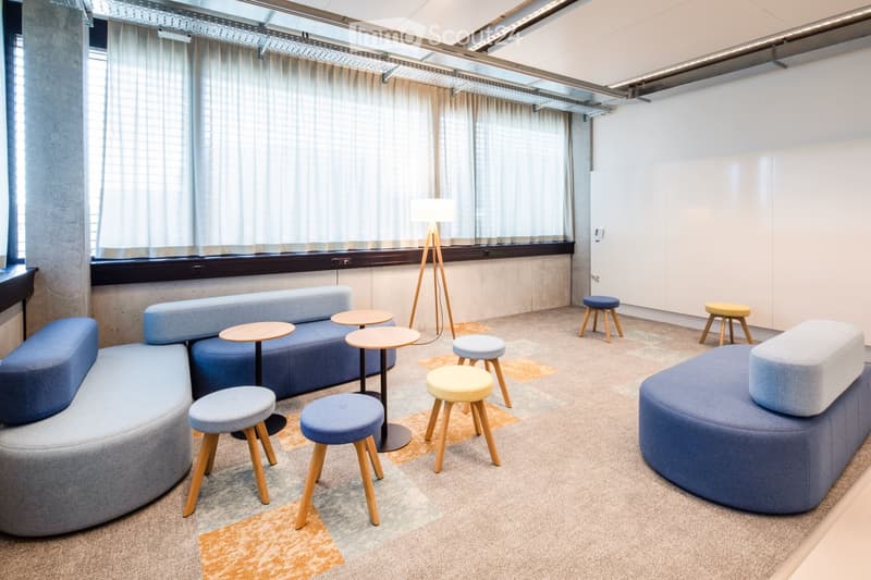 Modern, minimalist room with a curved blue sofa, small round tables, colorful stools, and a floor lamp near large windows with curtains.