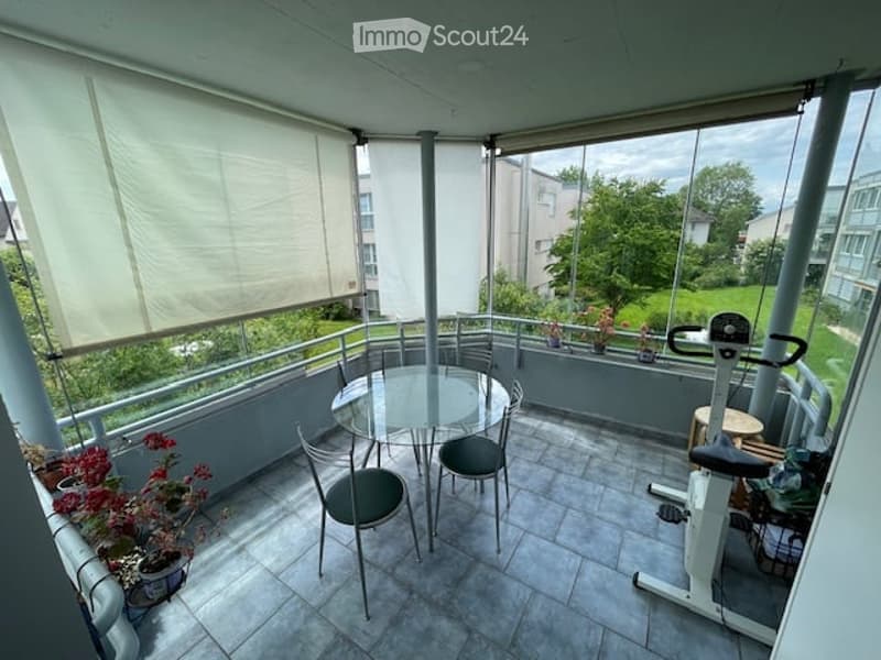 Balcony with table and chairs, exercise bike, potted plants, glass railings, shade covers