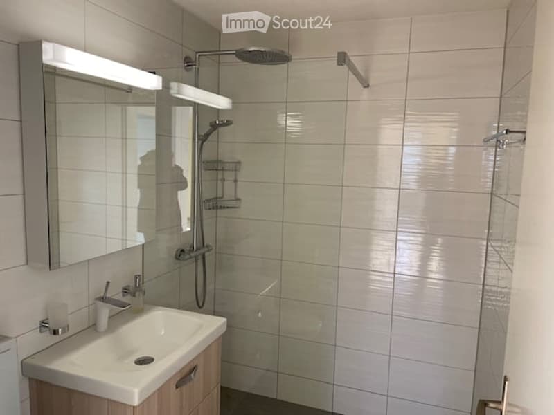 modern bathroom with white tiles, glass shower enclosure, white sink, mirror, and shower head