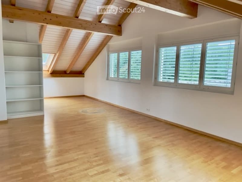 Completely empty room with wooden floor, white walls, large windows, and exposed wooden beams on the ceiling.