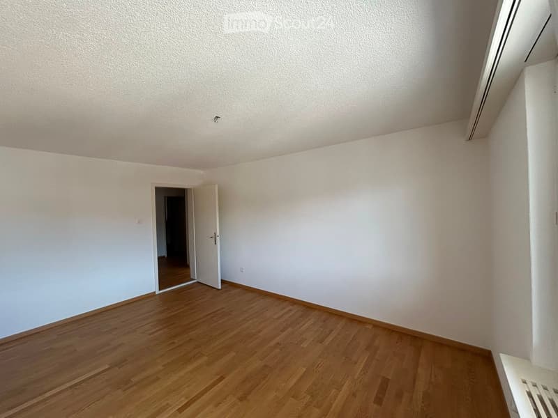 Empty room with white walls, wooden floor, and an open door leading to another space.