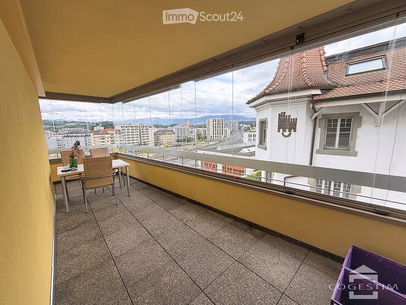 Balcony with tiled floor, glass railing, and a view of the cityscape. Includes a small table and chairs.
