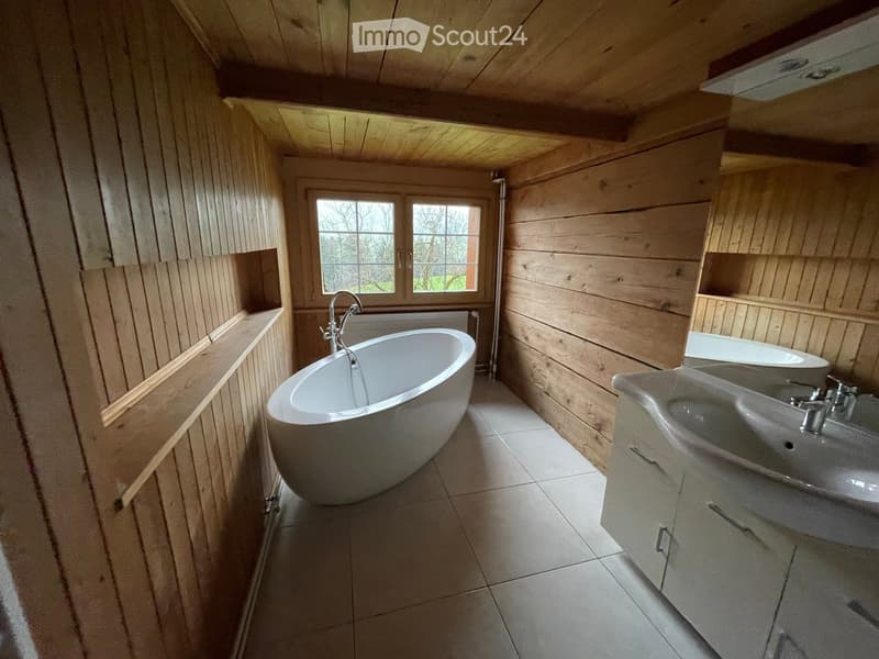 Bathroom with wooden walls and ceiling, featuring a freestanding bathtub, a double sink, and a window providing natural light.
